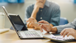 Duas pessoas analisando dados em laptop e calculadora.