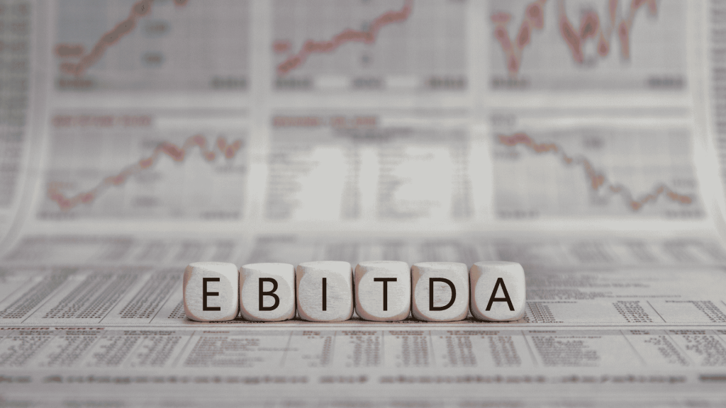 Letras formando a palavra EBITDA sobre relatórios financeiros e gráficos de desempenho empresarial