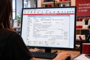 Pessoa operando computador em ambiente de loja varejista com a tela do sistema ERP Resulth Business aberta na aba de cadastro de clientes, destacando o campo de CNPJ preenchido no novo formato de CNPJ alfanumérico (A1B2C3D4/0001-9Z).